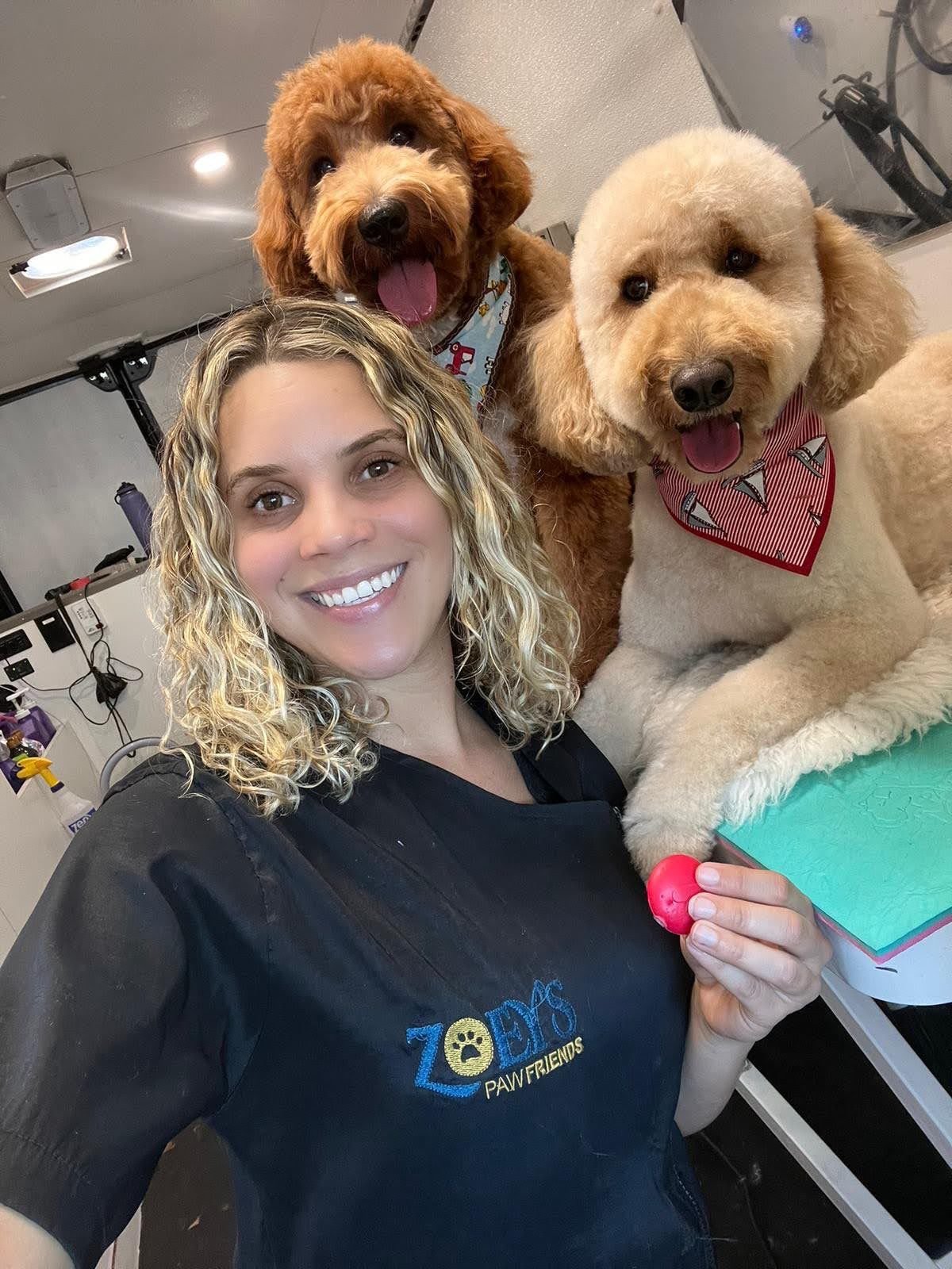 Expert female pet groomer Wanessa Medeiros smiling with two dogs inside a mobile grooming van in Los Angeles.