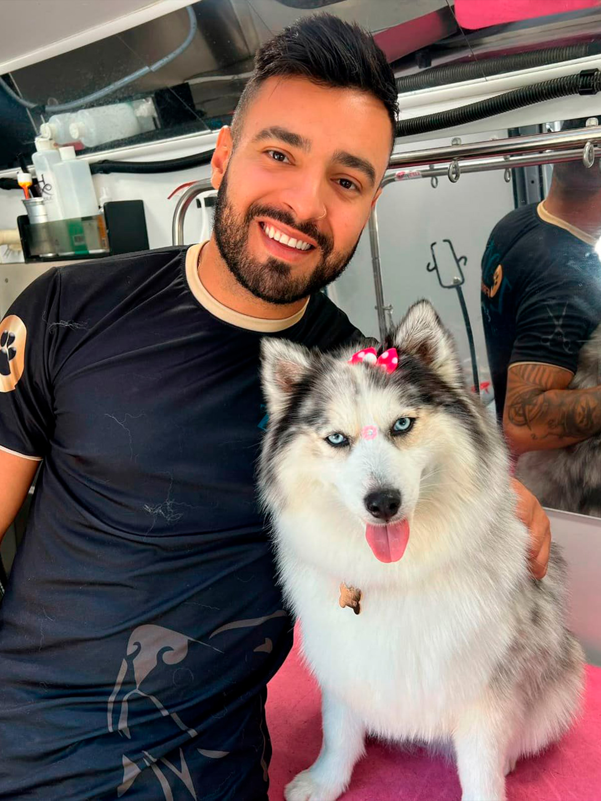 Professional pet groomer Henrique with a beautiful husky wearing pink bows after a mobile spa treatment in Austin, Texas.
